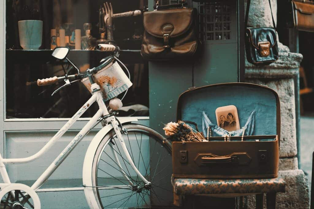 Vintage bicycle with open suitcase and bags outside a shop.